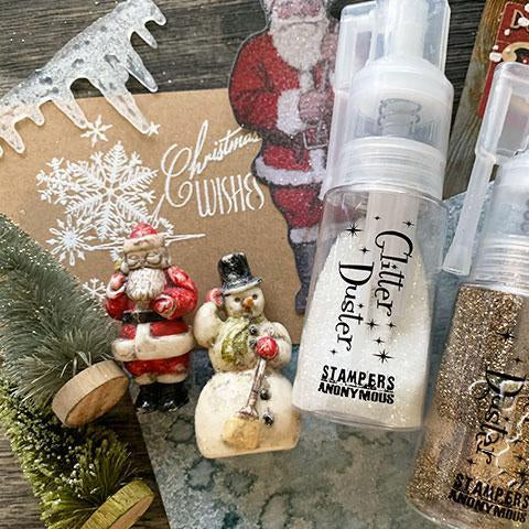 Two glitter dusters with 'Stamper Anonymous' branding on a festive background with Christmas decorations.