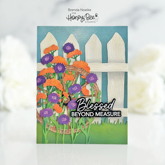 Handmade card featuring purple and orange paper flowers against a white picket fence.