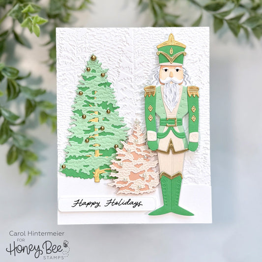 Handmade holiday card featuring a green nutcracker and two festive trees on textured white paper.