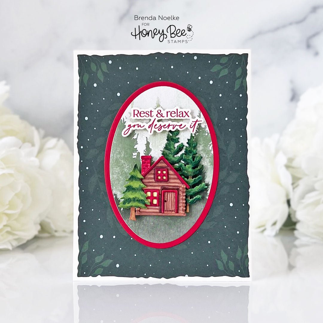 Handmade card with a red cabin, evergreen trees, and the text 'Rest & relax you deserve it'.
