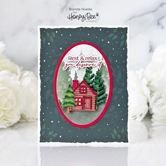 Handmade card with a red cabin, evergreen trees, and the text 'Rest & relax you deserve it'.