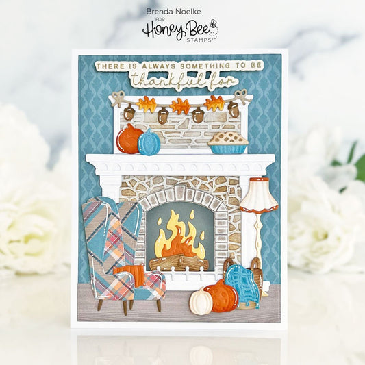 Handmade fall greeting card featuring a cozy fireplace scene with a plaid chair and pumpkins.