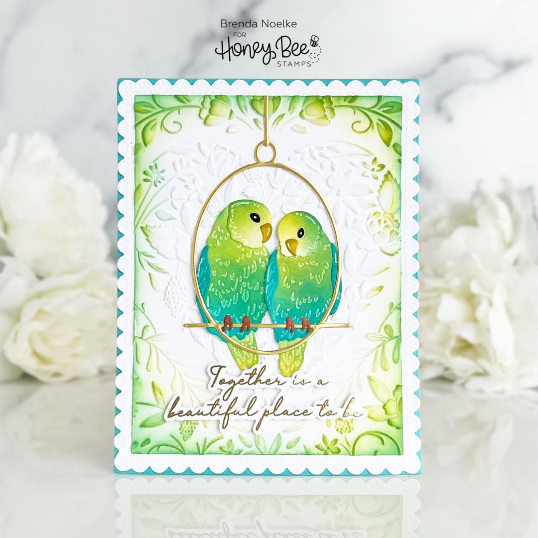Handmade card featuring two green lovebirds in a golden hoop with floral accents.