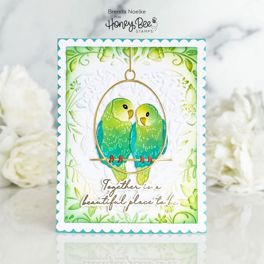 Handmade card featuring two green lovebirds in a golden hoop with floral accents.