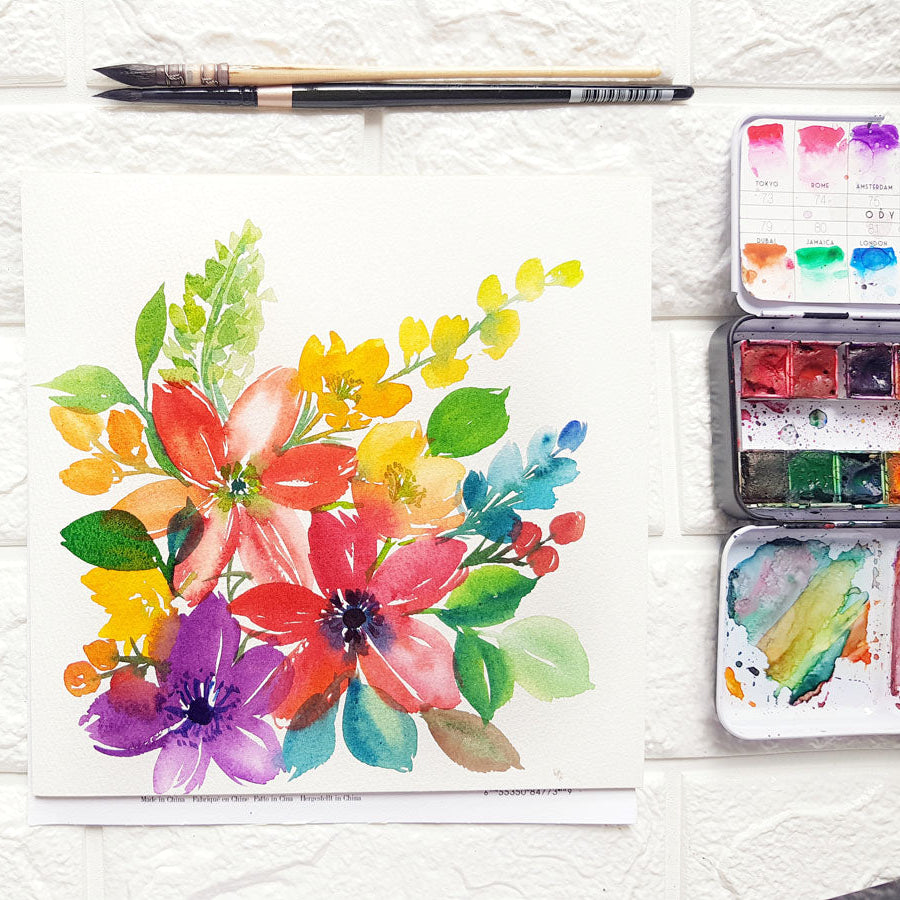 Colorful watercolor floral painting on a textured surface with a paintbrush and watercolor set.