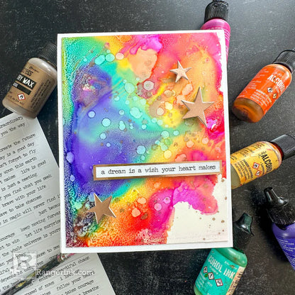 Colorful art card with star decorations and text, surrounded by art supplies on a dark surface.