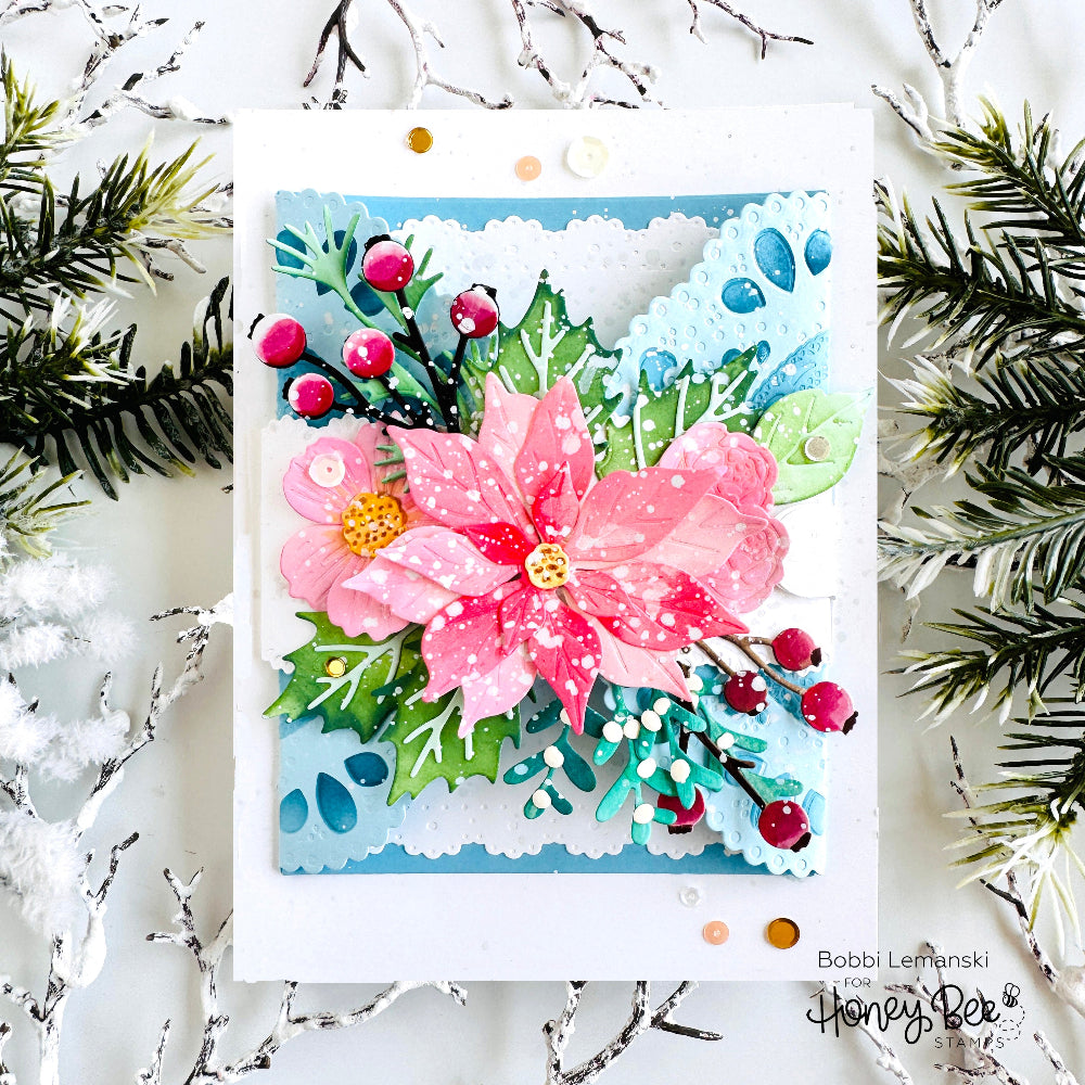 A handmade layered paper card featuring a pink poinsettia, green holly leaves, red berries, and blue scalloped borders, styled with pine branches on a white background. The card is signed by Bobbi Lewanski and Honey Bee Card Company.