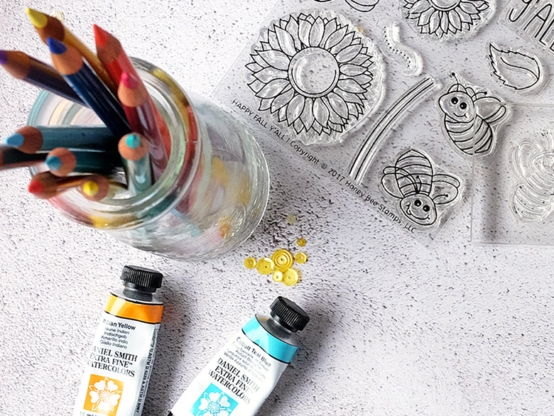 Art supplies including colored pencils, paint tubes, and stencils on a textured surface.
