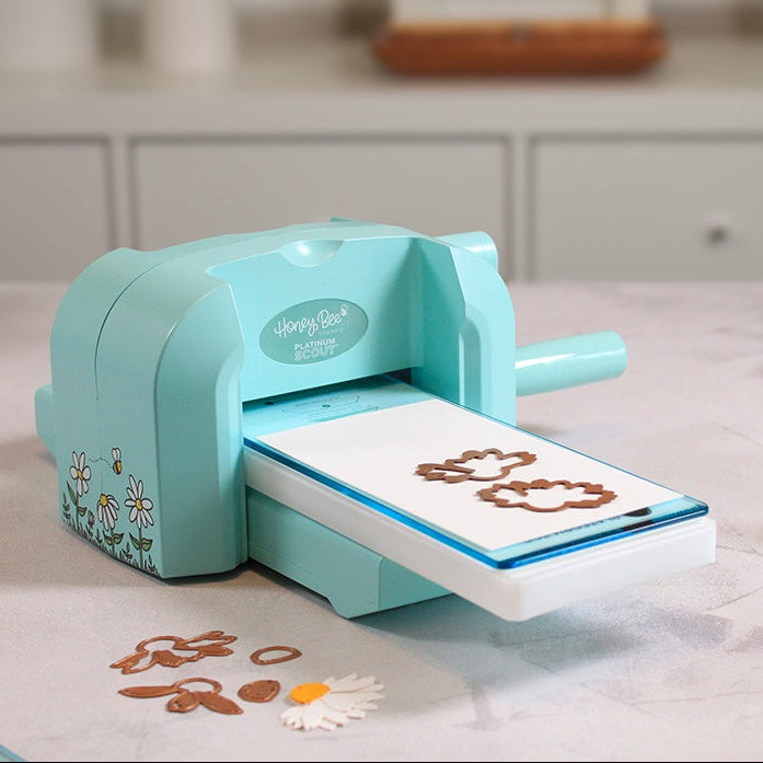 Bee Creative Platinum Scout die cutting machine in teal with cutting plates loaded and die-cut flower pieces on a counter
