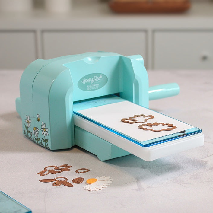 Bee Creative Platinum Scout die cutting machine, angled view with plates in the slot and die-cut daisy pieces in front