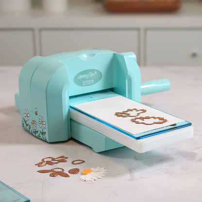 Bee Creative Platinum Scout die cutting machine, angled view with plates in the slot and die-cut daisy pieces in front