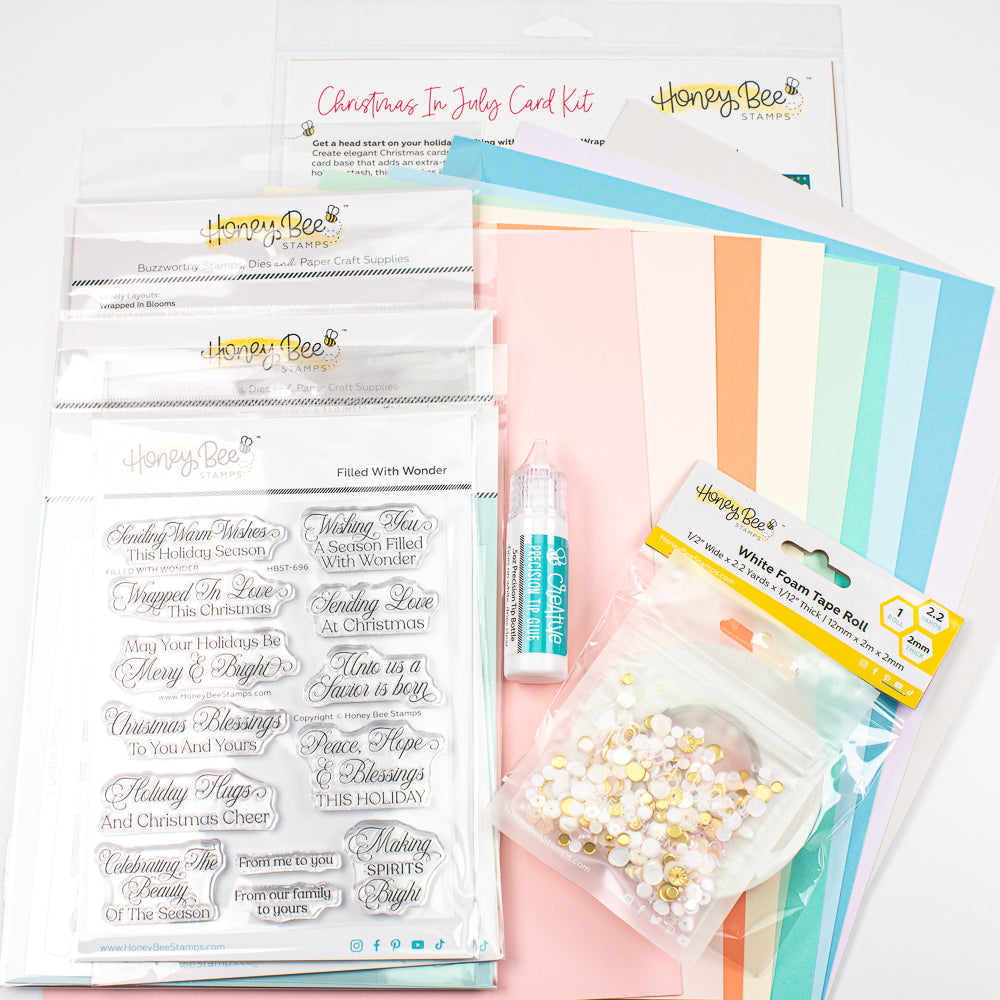 A collection of craft supplies from Honey Bee Papercraft, including a Christmas in July card kit, white flower tape buds, clear stamps, and pastel striped cardstock sheets, arranged on a white background.