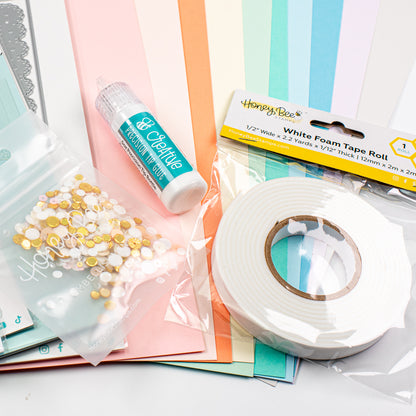 A craft supply bundle featuring a roll of white foam tape, a tube of gel nail polish remover, a bag of gold and white sequins, and colorful striped paper sheets on a white background.