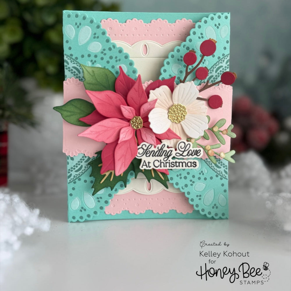 A handmade layered Christmas greeting card with pink poinsettias, a white daisy, green leaves, and red berries on a turquoise and pink scalloped background. The card is displayed on a white surface with a blurred holiday background, featuring a Honey Bee Stamps logo in the bottom right corner.