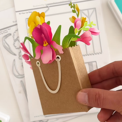 Hand holding a small brown paper bag with colorful paper flowers on top