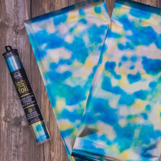 Decorative foil with blue and yellow pattern next to a can of spray foil on a wooden surface