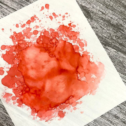 Red watercolor stain on a white paper sheet with a gray wooden background
