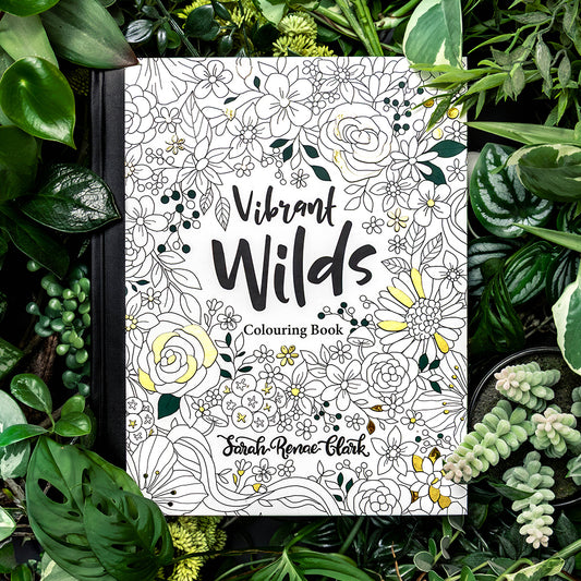 Coloring book titled 'Vibrant Wilds' surrounded by green plants